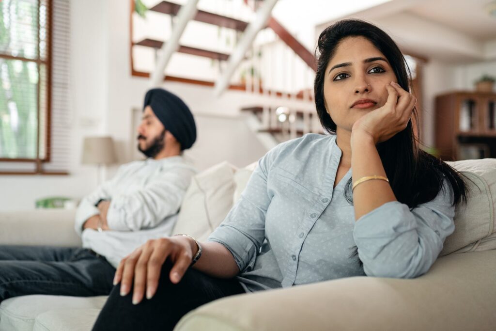 Sad young Indian woman avoiding talking to husband while sitting on sofa