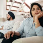 Sad young Indian woman avoiding talking to husband while sitting on sofa