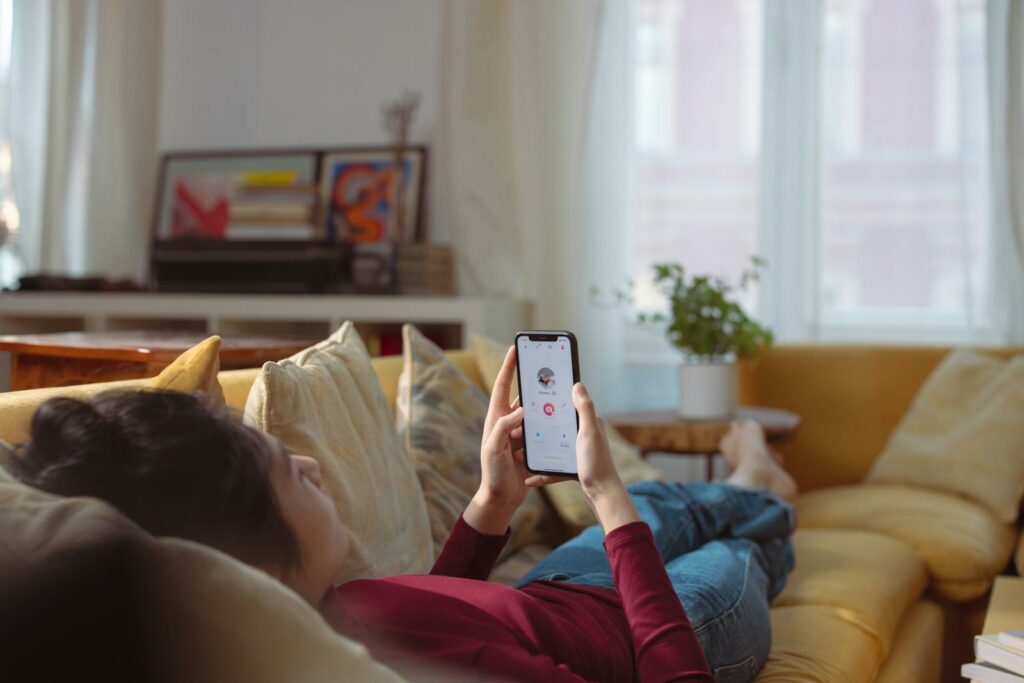 A Person Lying on Sofa Holding a Smartphone with a Person's Profile on Screen